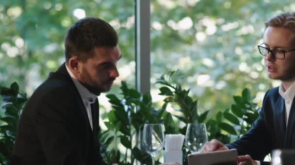 Dos hombres de negocios con trajes conversan y llegan a un acuerdo con un apretón de manos en un restaurante . — Vídeo de stock