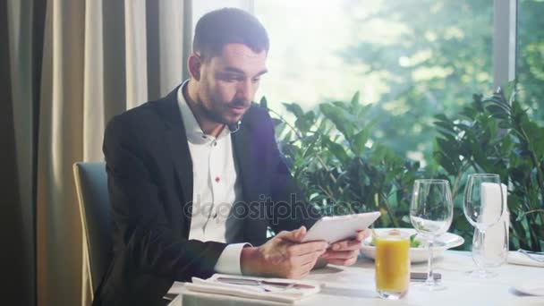 Empresário em um terno está feliz em ver resultados de sucesso em um tablet em um restaurante . — Vídeo de Stock