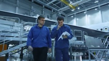 İki uçak bakım mekanik bir uçak hangar gazetelerde arka planda bir uçak ile kontrol ederken bir görüşme.