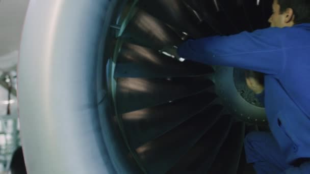 Meccanico di manutenzione aeronautica con una luce flash ispeziona pale di turbina piana in un hangar . — Video Stock