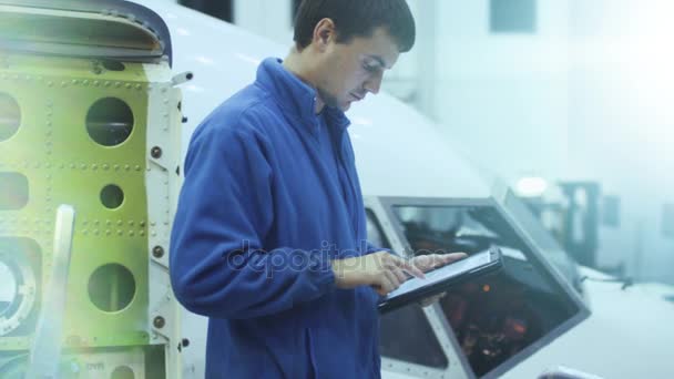 Mecánico de mantenimiento de aeronaves utiliza tableta delante de una cabina de avión en un hangar . — Vídeos de Stock