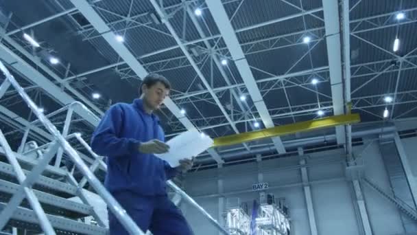 Meccanico di manutenzione aeronautica in uniforme blu sta scendendo le scale durante la lettura di carte in un hangar . — Video Stock