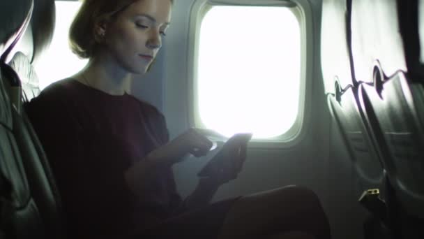 Genç kadın bir pencere yanında bir smartphone içinde bir uçak kullanıyor. — Stok video