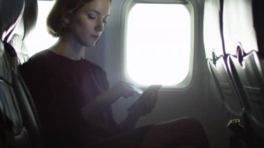Genç kadın bir pencere yanında bir smartphone içinde bir uçak kullanıyor.