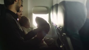 Bir çocuk ile genç aile içinde bir uçak bir pencere yanında oturup bir oyuncak ayı ile oynamak.