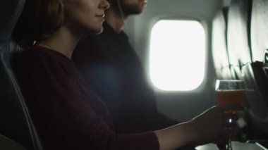 Genç kadın bir uçakta bir kokteyl içiyor ve bir adam bir pencere yanında arka planda müzik dinlemek.