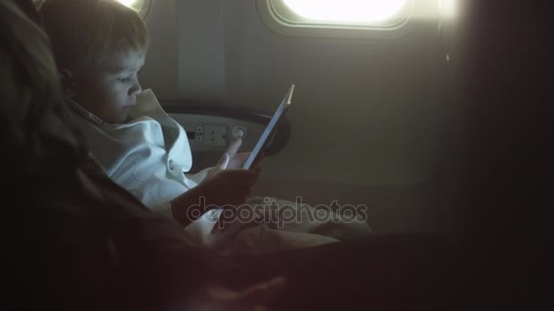 El niño está jugando con la tableta en un avión al lado de una ventana . — Vídeos de Stock