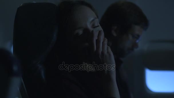 Ung kvinna sover på ett flygplan och en man sitter i bakgrunden bredvid ett fönster. — Stockvideo