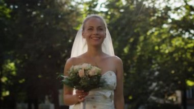 Genç gelin bir gelinlik açık havada bir güneşli parkta hareket ediyor.
