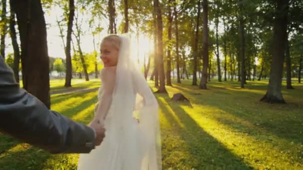 Sonriente novia sostiene novio por la mano y corre en un parque . — Vídeo de stock