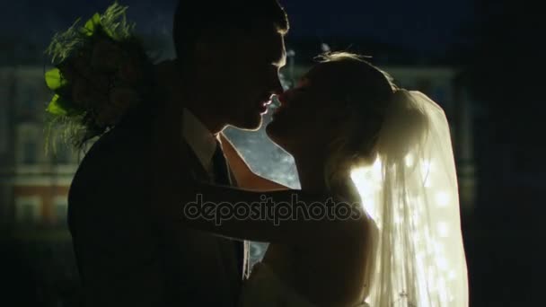 Joyeux jeunes mariés s'embrassent à côté de feux d'artifice dans un parc le soir .