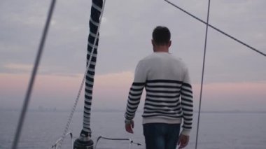 Adam bir yelkenli deniz üzerinde rahatlatıcı bir şekilde el yükseltir.