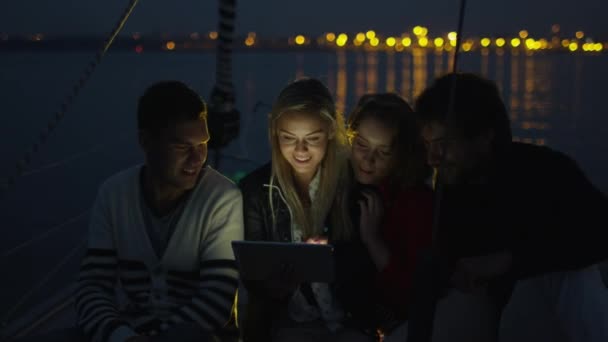 Un grup de oameni folosesc tableta pe o barcă cu vele în mare noaptea. . — Videoclip de stoc