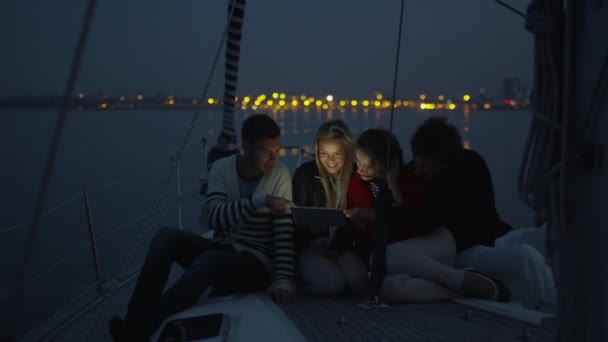 人々 のグループは夜海でヨットの上でタブレットを使用しています。. — ストック動画