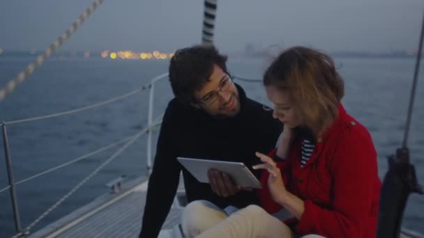 カップルが海でヨットの上でタブレットを使用してください。. — ストック動画