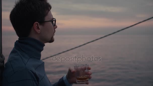 Νεαρός άνδρας με ένα ποτήρι ουίσκι σε ένα γιοτ στη θάλασσα. — Αρχείο Βίντεο