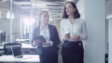 İki çekici kadın işçi ofis aracılığıyla yürüyor. Bir tanesi Tablet Pc holding.