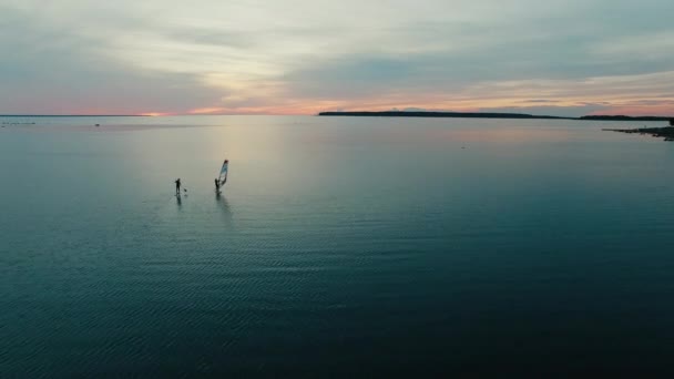 Aerial drone shot of windsurfer and paddleboarder at sunset. — Stock Video