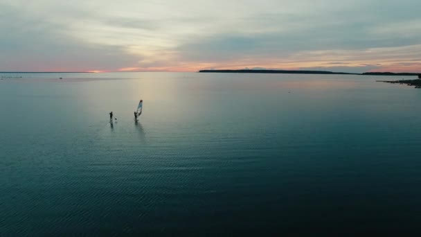 Antenn drönare skott av vindsurfare och paddleboarder vid solnedgången. — Stockvideo