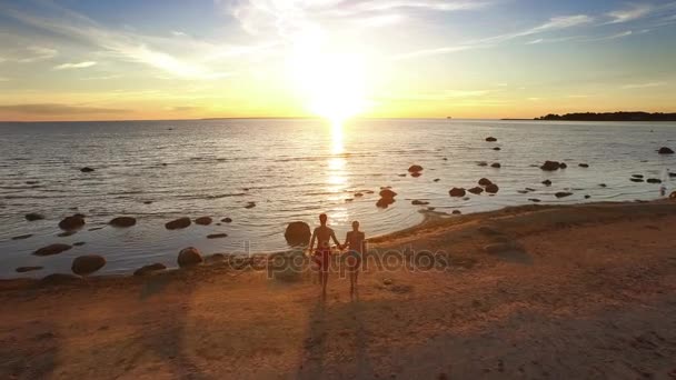 Drone aéreo tiro de um casal correndo para a água ao pôr do sol . — Vídeo de Stock