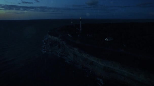 Luchtfoto drone nacht shot van een vuurtoren in de regen op een klif. — Stockvideo