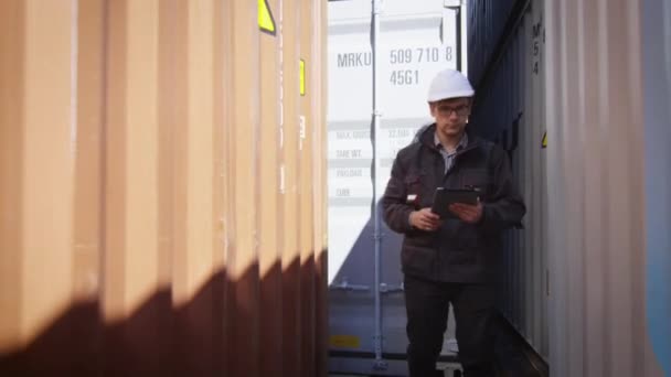 Lavoratore in Hard Hat sta camminando con Tablet PC tra i contenitori nel centro logistico — Video Stock