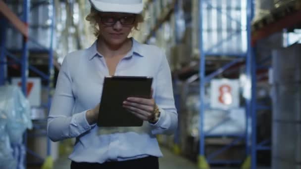 Mujer Gerente en Hard Hat Walking in Logistic Warehouse. Mantener la tableta PC en las manos . — Vídeo de stock