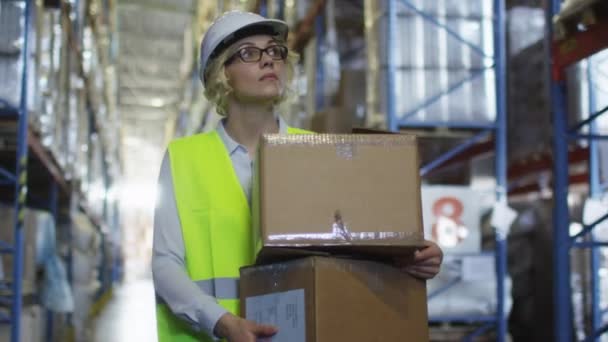 Ženské pracovník logistického skladu je chůze mezi policemi. Kartonové krabice v rukou drží. — Stock video