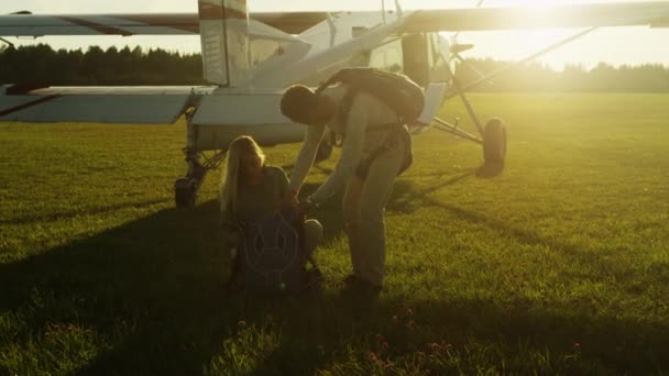 Мужчина помогает девушке надеть парашют перед полетом — стоковое видео