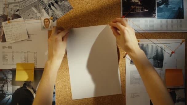 Detective puts a piece of paper on evidence pinboard with clues and suspects. — Stock Video