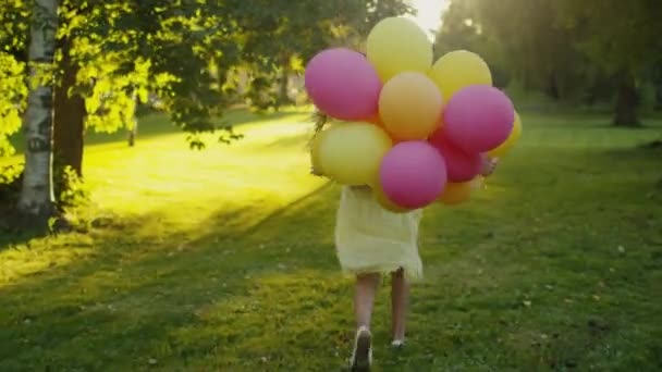 Chica está corriendo en el parque con globos en la mano al atardecer — Vídeo de stock