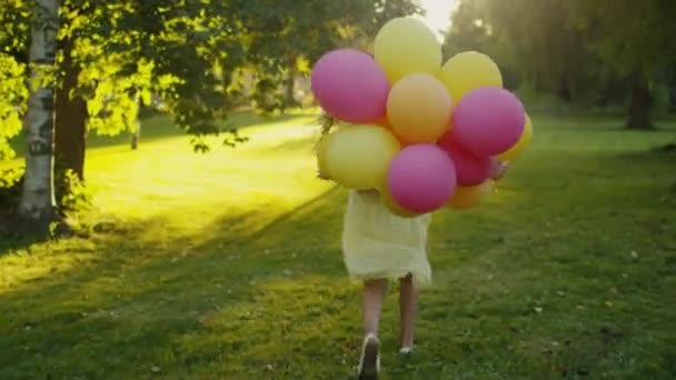 La fille court au parc avec des ballons à la main à l'heure du coucher du soleil — Video