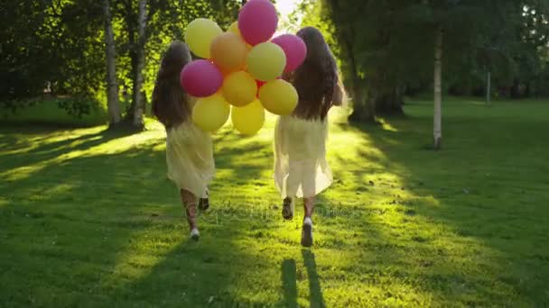 Zwillingsmädchen läuft im Park mit Luftballons in der Hand bei Sonnenuntergang — Stockvideo