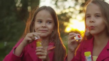 İki ikiz kız sabun köpüğü ile parkta oynuyorlar