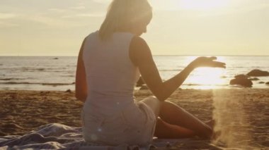 Sahilde oturan ve oyun kum günbatımı ışık ile genç kız beyaz bez içinde