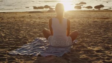 Genç sarışın kız meditasyon Lotus poz sahilde günbatımı ışık içinde