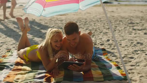 Jovem casal sorrindo está usando Tablet PC na praia no dia ensolarado — Vídeo de Stock