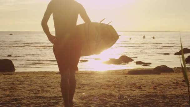 Homme avec planche de surf court dans l'eau à la lumière du coucher du soleil — Video