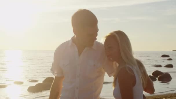 Pareja feliz y relajada caminando en la playa bajo la luz del atardecer . — Vídeo de stock