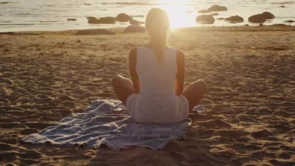 Joven rubia está meditando en la postura del loto en la playa bajo la luz del atardecer — Vídeo de stock