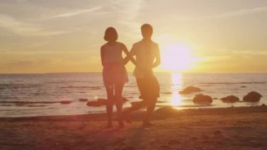 Kız ve adam sahilde birlikte eğleniyor. Elele ve gün batımı zamanında döne döne.