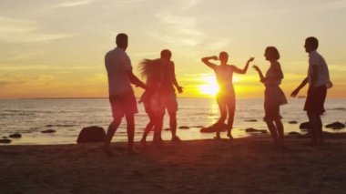 Bir grup genç insan vardır Dancing sahilde günbatımı ışığı