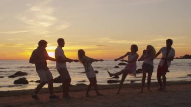 Bir grup genç insan eğleniyor sahilde günbatımı zaman.