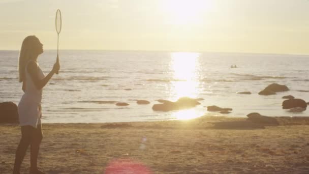 女孩和男人玩羽毛球海滩，日落时间 — 图库视频影像
