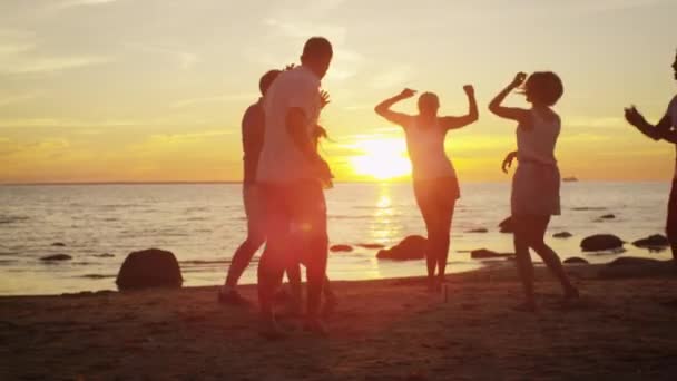 Grupo de jóvenes felices bailan en la playa bajo la luz del atardecer — Vídeos de Stock