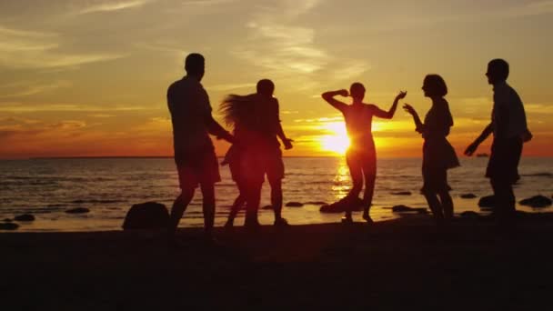 Grupo de jóvenes felices bailan en la playa bajo la luz del atardecer — Vídeo de stock