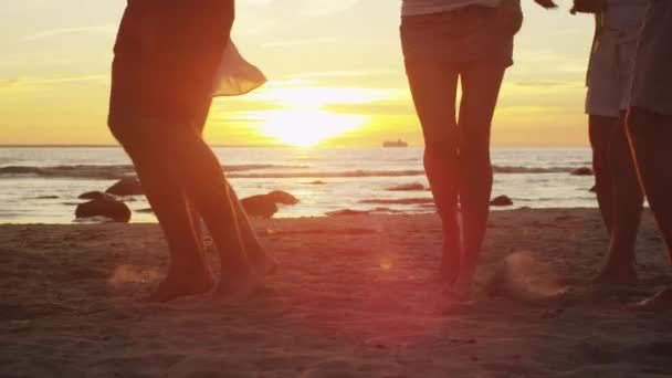 Benen van gelukkige jonge mensen zijn dansen op het strand bij zonsondergang licht. Slow Motion 60 Fps. — Stockvideo