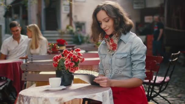 Menina sorridente está usando tablet no café ao ar livre — Vídeo de Stock
