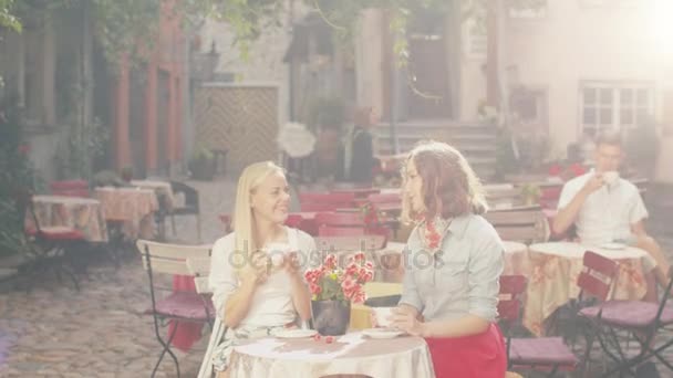 Две девушки разговаривают в кофейне на открытом воздухе — стоковое видео