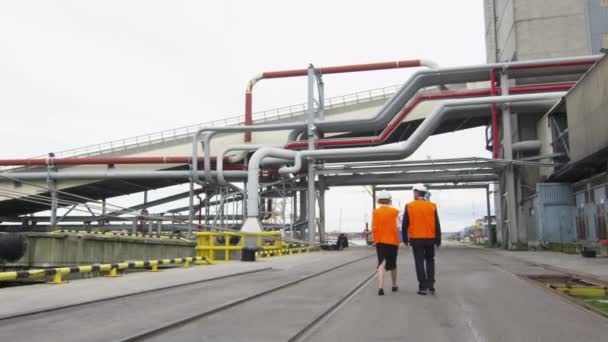 Gente de negocios en chalecos de seguridad y sombreros duros están caminando en un entorno industrial . — Vídeo de stock